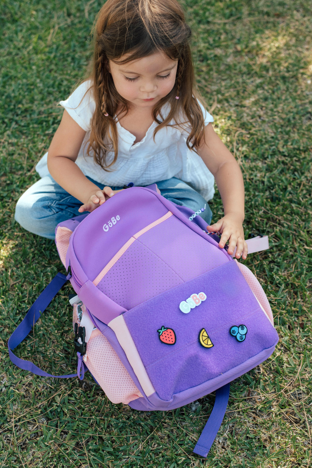 Child sitting on grass with a purple backpack featuring colorful patches