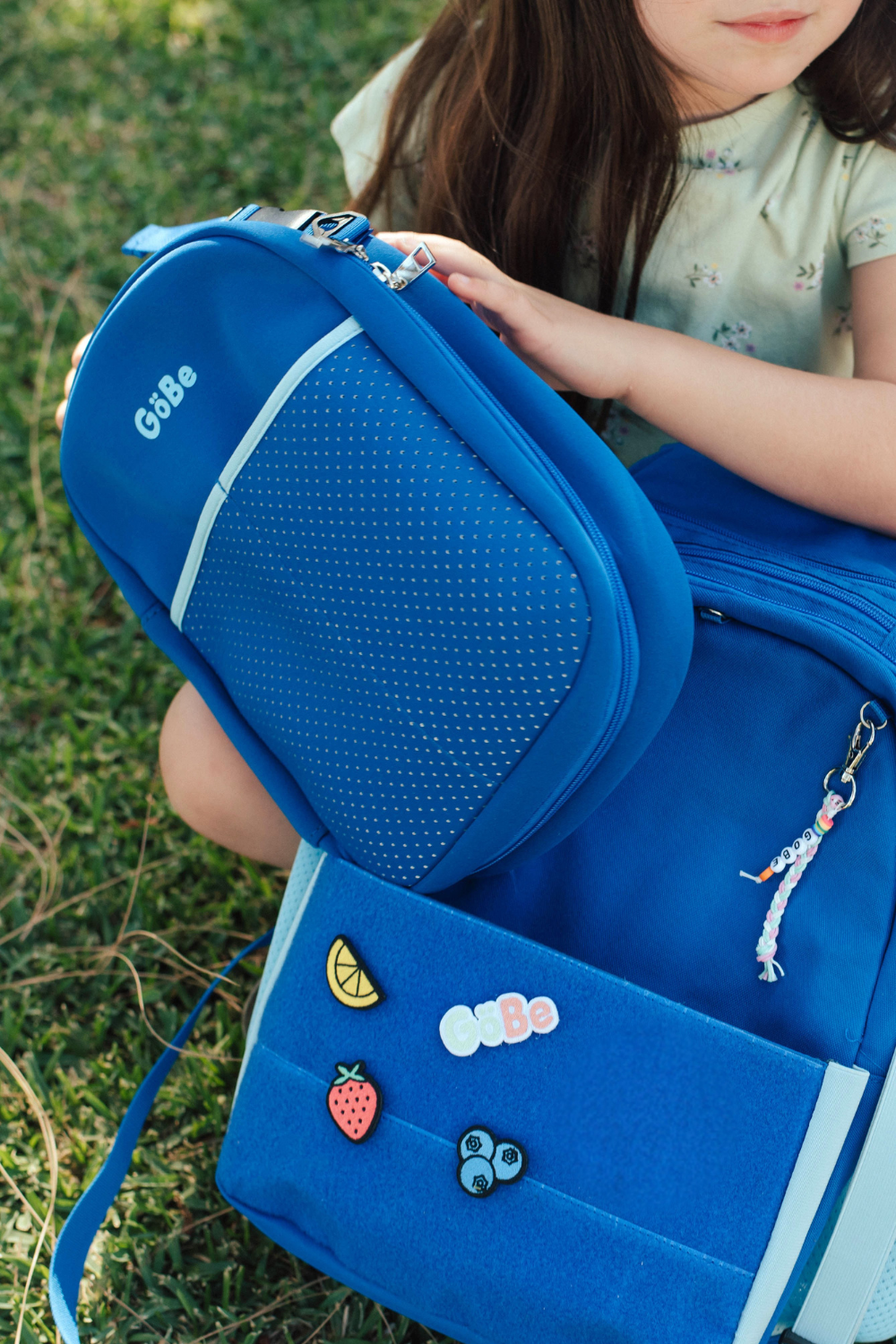 Blue backpack with colorful patches held by a child sitting on grass