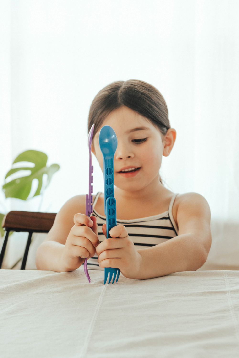 Young girl holding two colorful forks in front of a white background