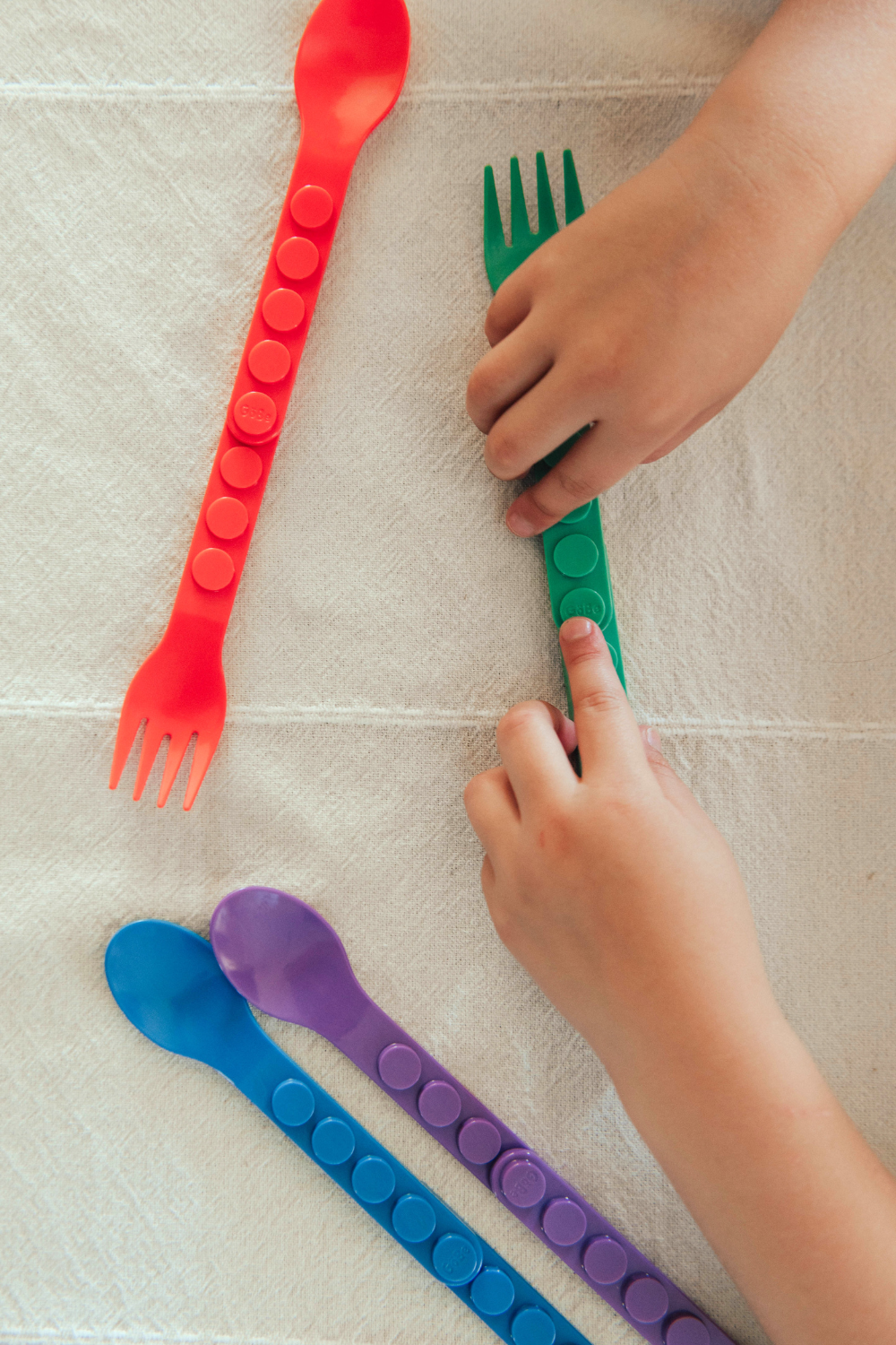 Colorful plastic utensils on a tiled floor with children&#39;s hands interacting with them.