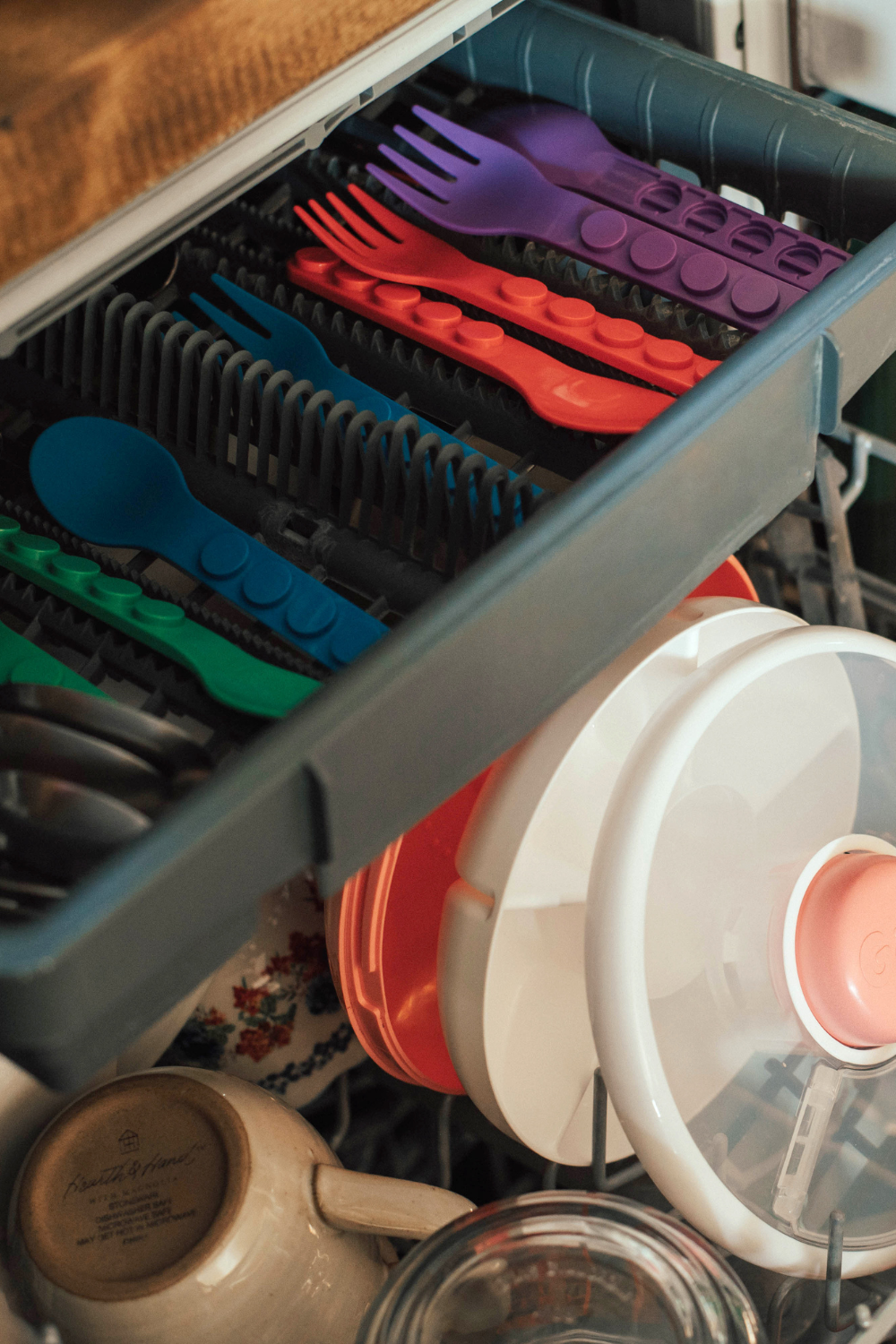 Dishwasher with a drawer open, showing colorful utensils and dishes.