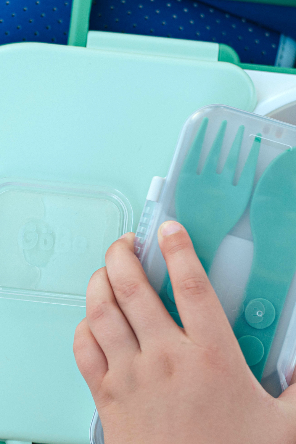 Hand holding a set of green plastic utensils with a blue container in the background