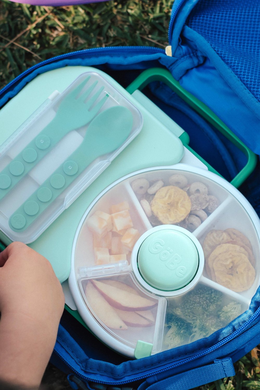 Children&#39;s lunchbox with compartments for food and utensils, outdoors.
