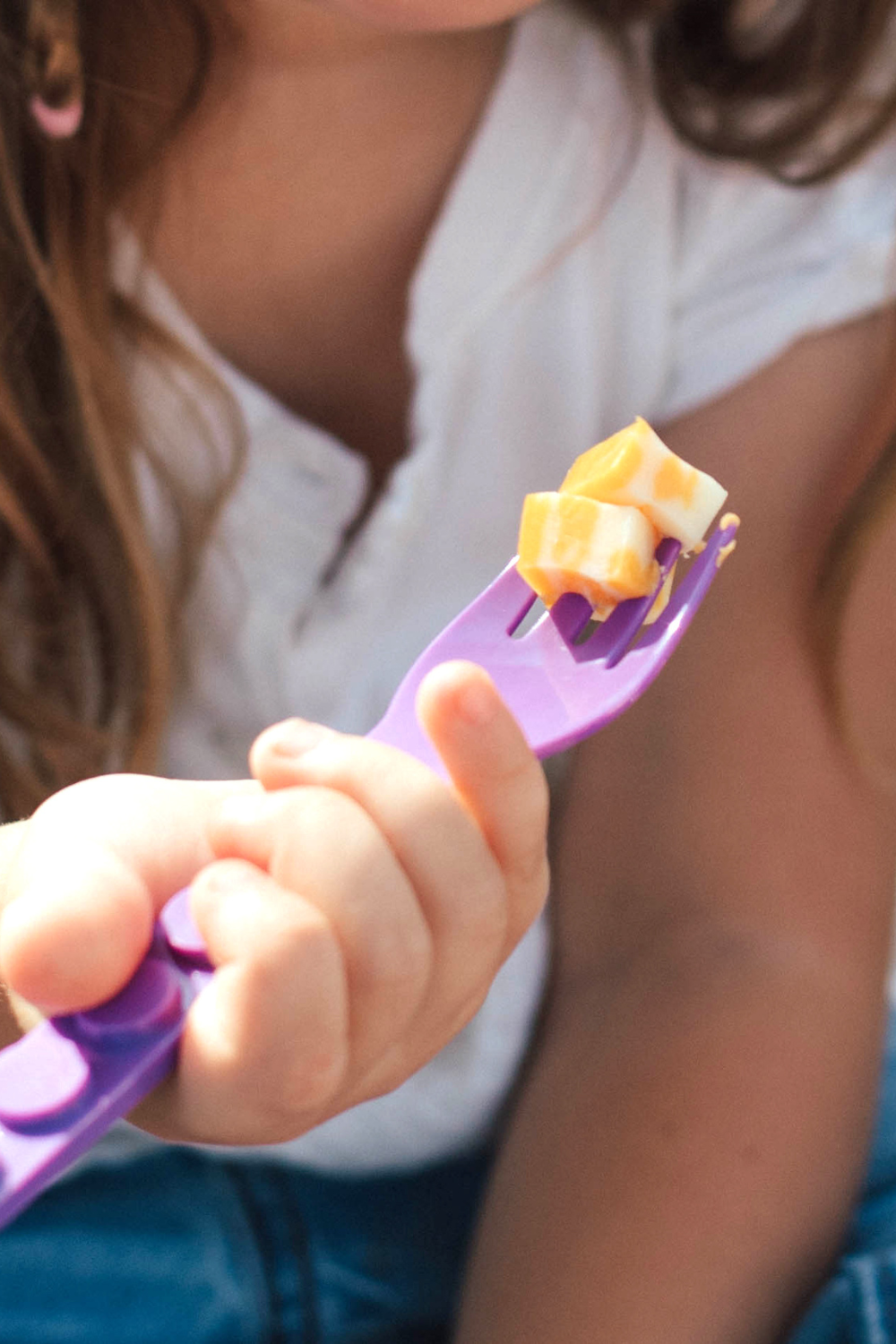 Child holding a purple fork with food on it