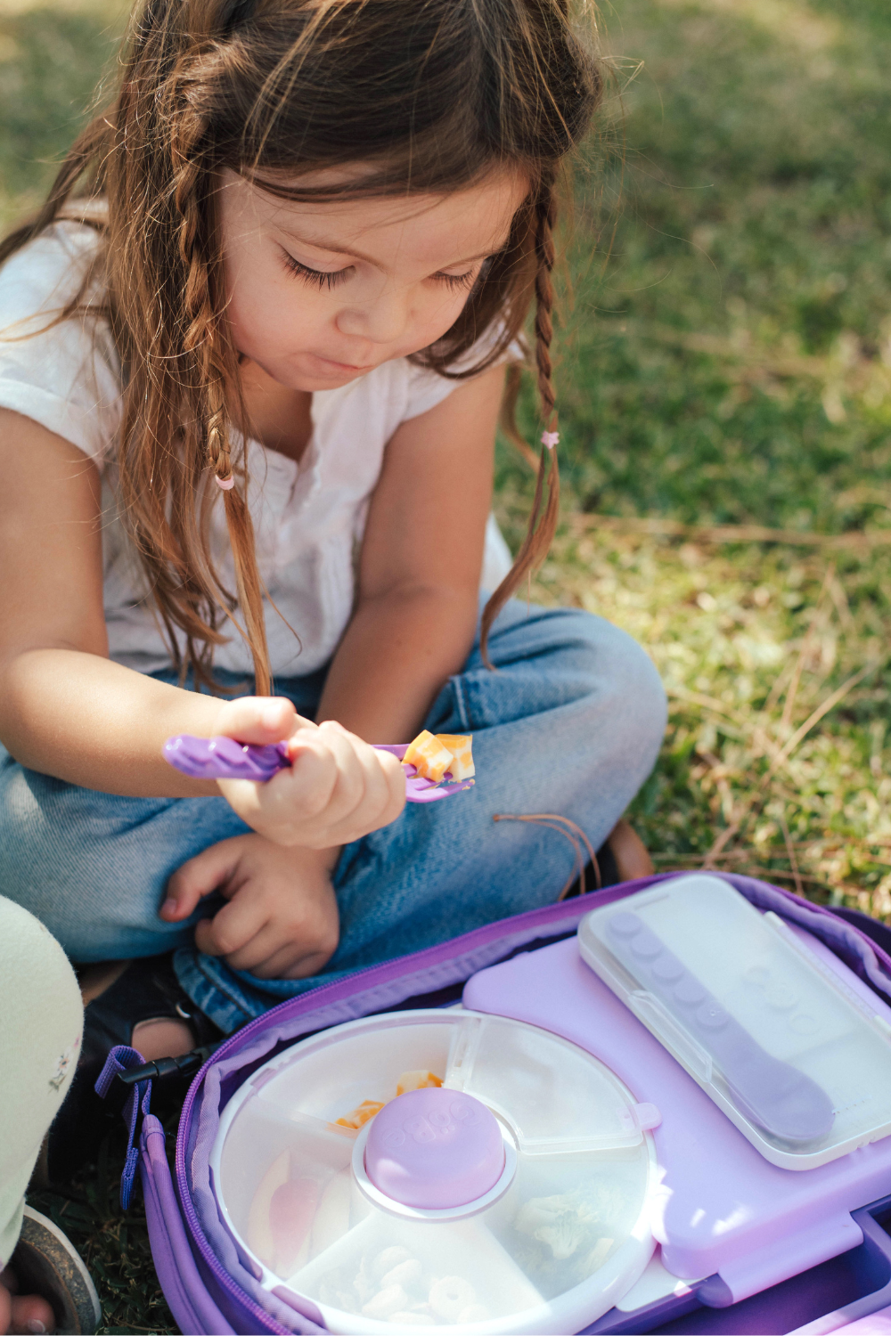 Child eating from a purple lunch box outdoors